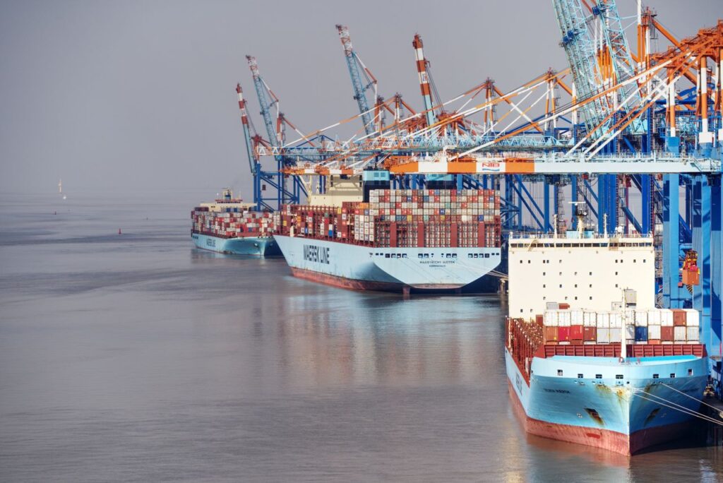 pexels-photo-11555089-11555089 Container ships docked at a busy port with vibrant cranes and clear skies.