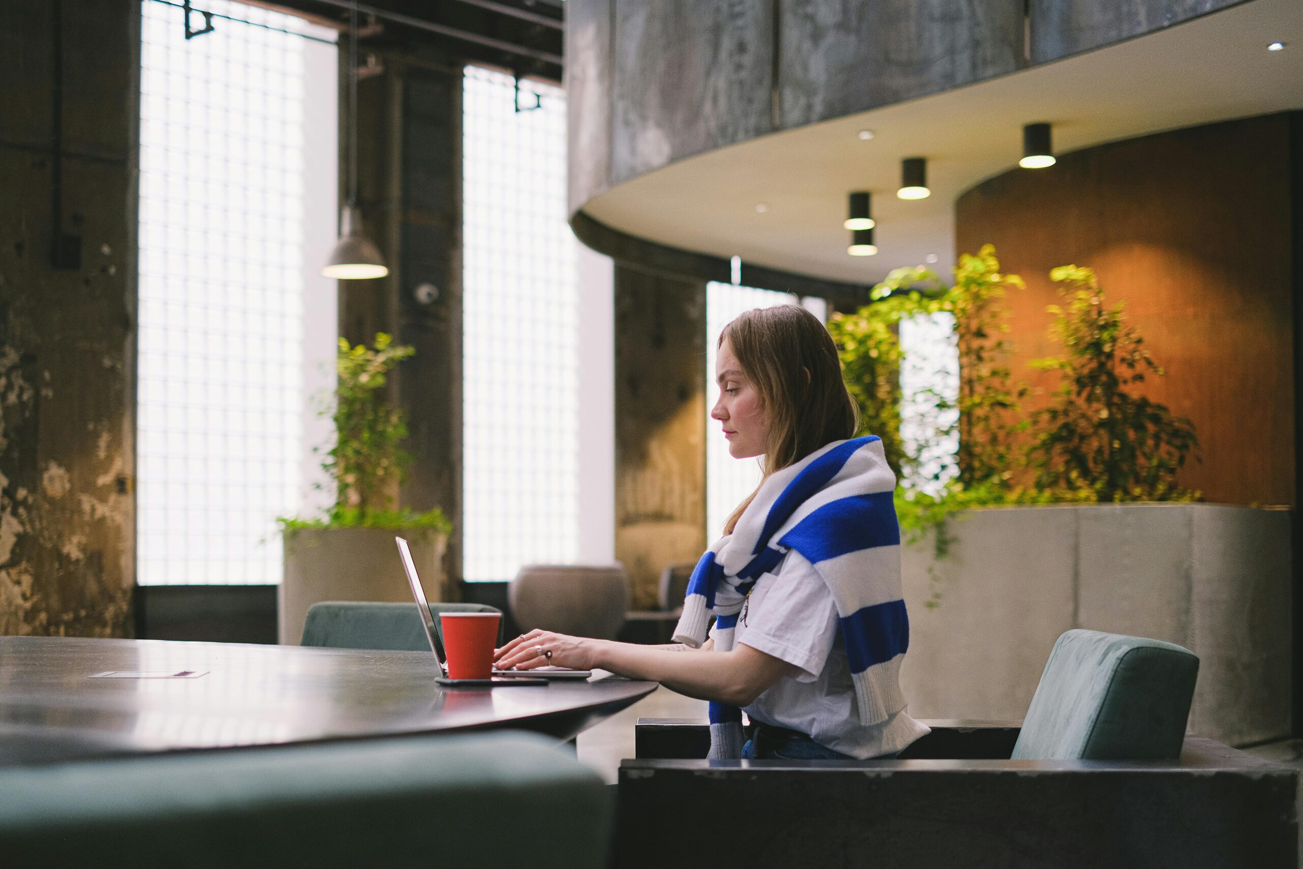 pexels-photo-12662807-12662807 Woman in a striped scarf works on a laptop indoors at a stylish, green workspace.