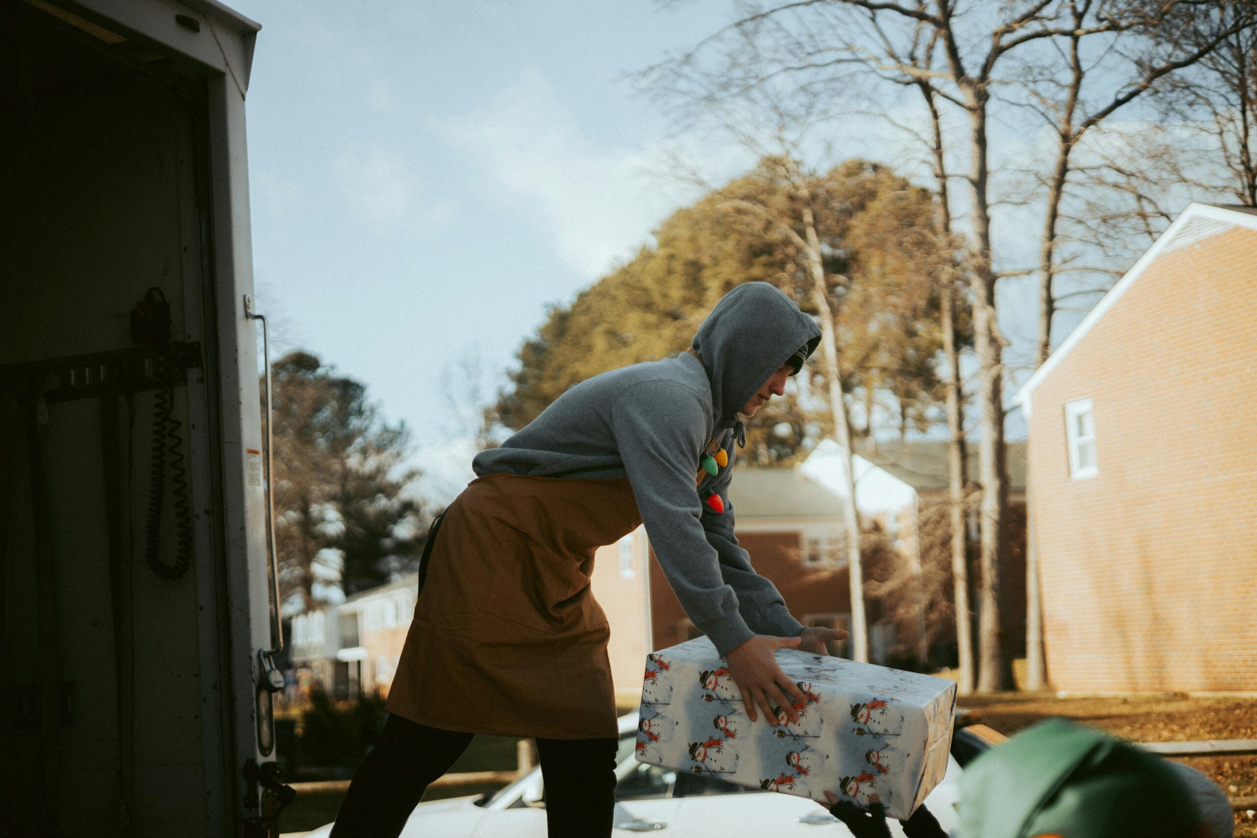 pexels-photo-14831688-14831688 A man in a hoodie unloads a festive gift box from a delivery truck during a community event.