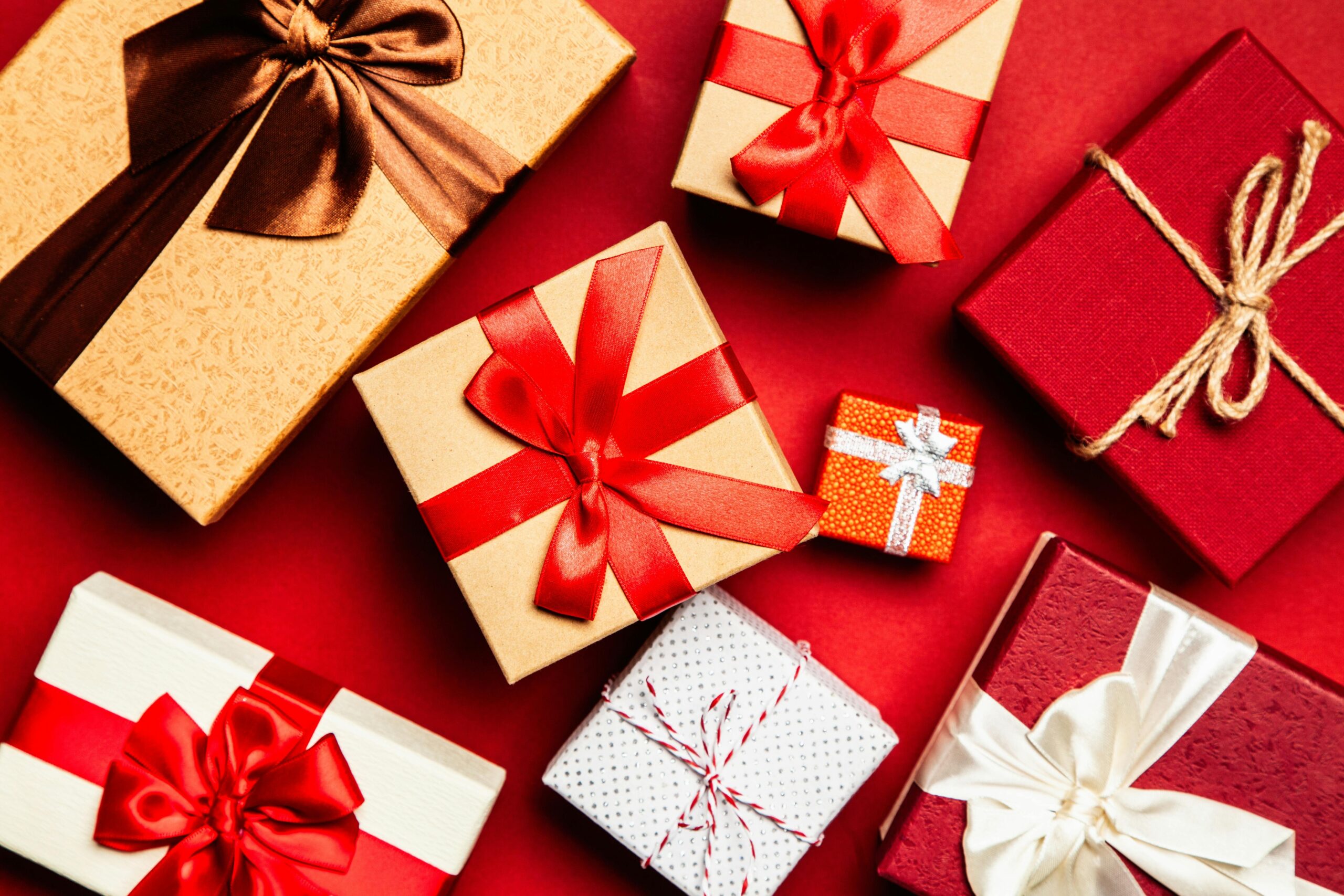 pexels-photo-1666065-1666065 Top view of beautifully wrapped holiday gifts with red and brown ribbons on a vibrant red background.