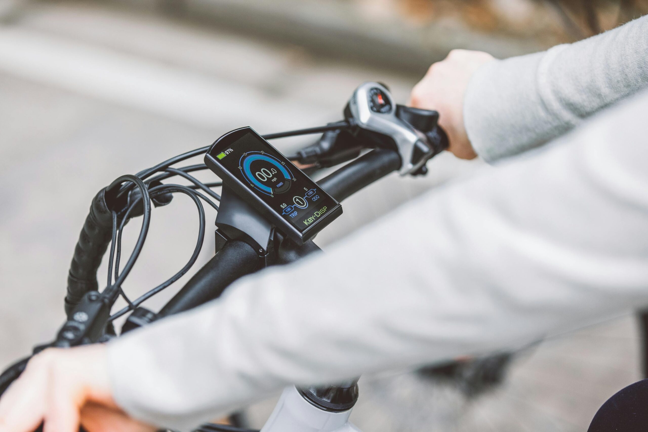 pexels-photo-19411386-19411386 Hands gripping the handlebar of an electric bicycle, showcasing the digital display screen for speed and battery status.