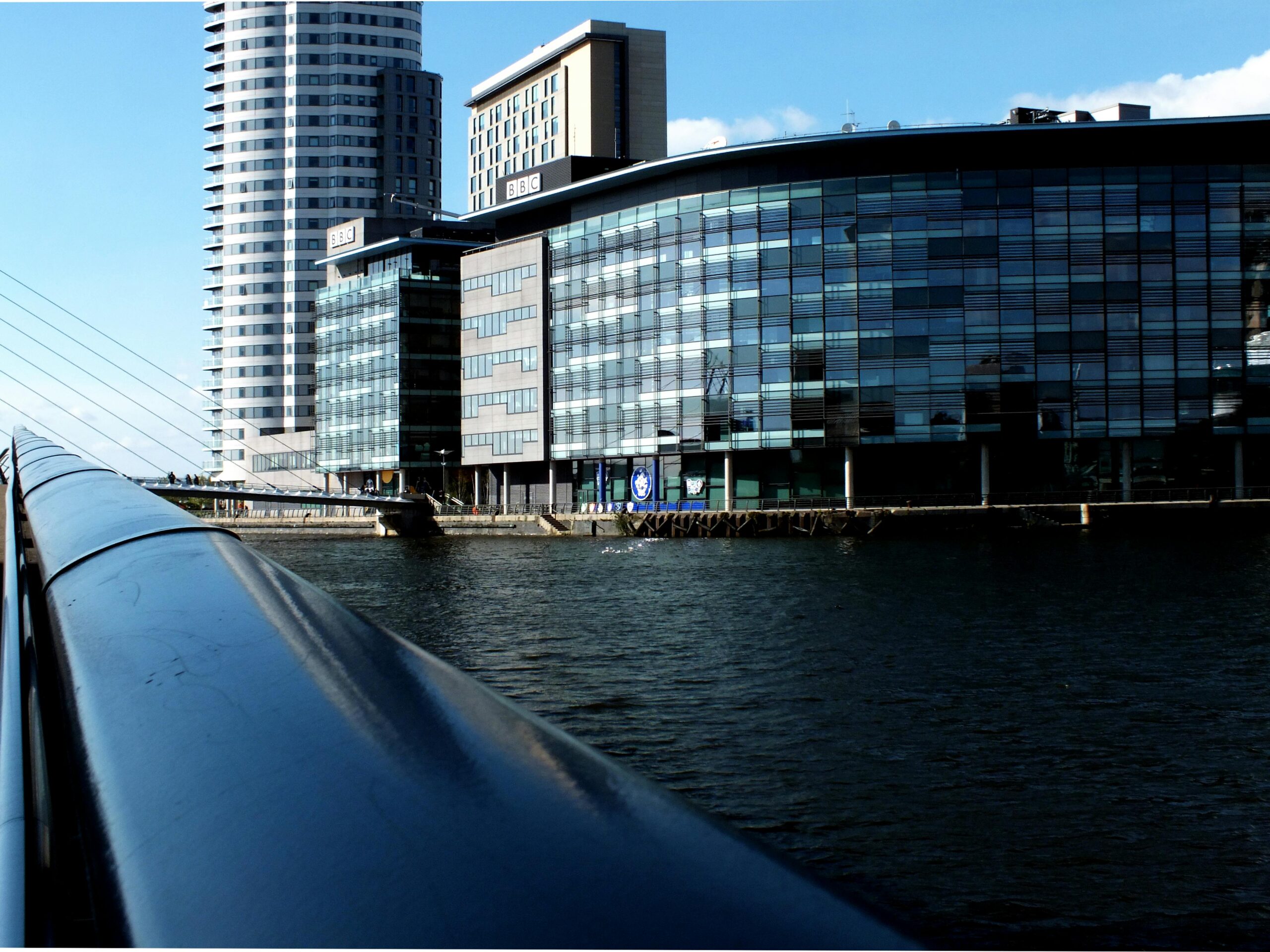 Reflection of skyscrapers and waterfront architecture in Manchester, UK under clear blue skies.