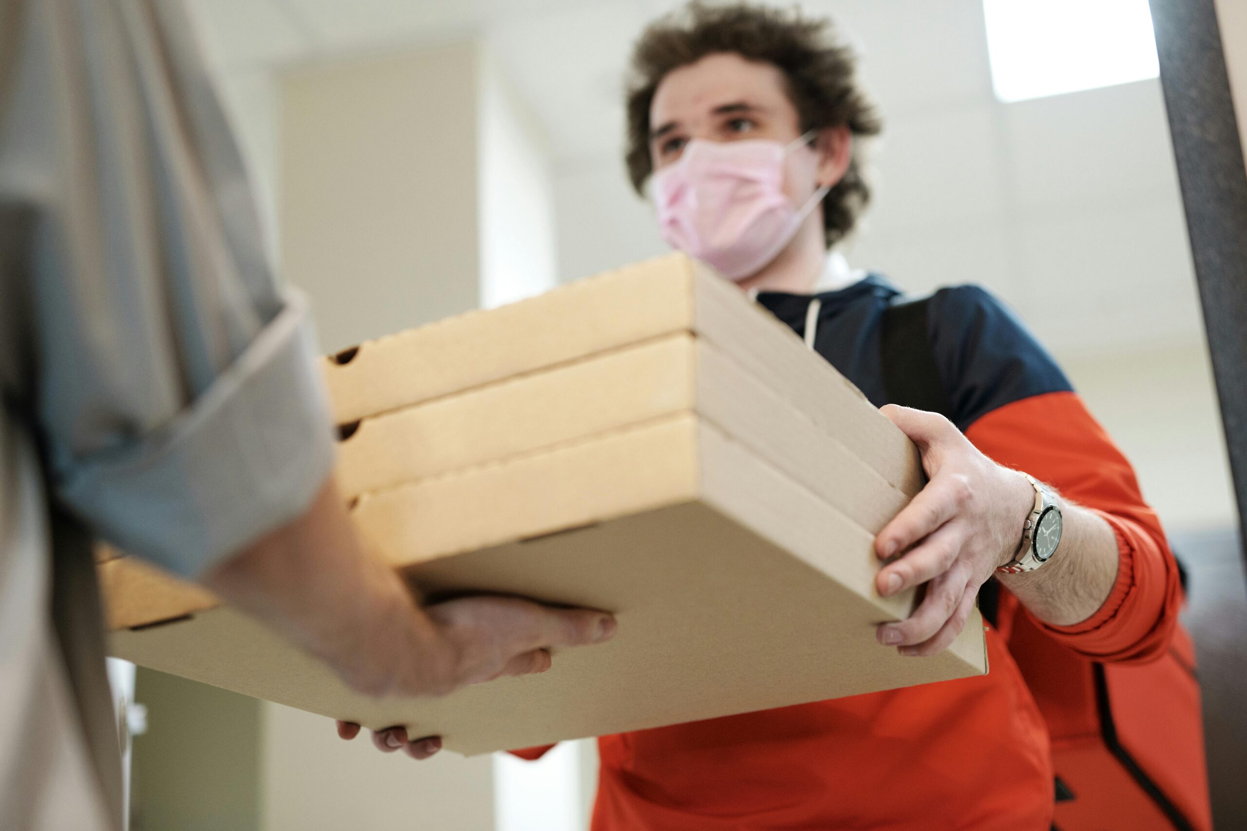 pexels-photo-4393426-4393426 Delivery worker handing over pizzas while wearing a protective mask indoors, illustrating safe delivery practices during a pandemic.