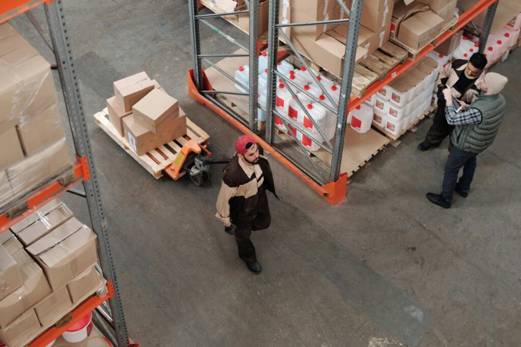 pexels-photo-4481259-4481259 Team working in an industrial warehouse discussing and organizing inventory with pallets.