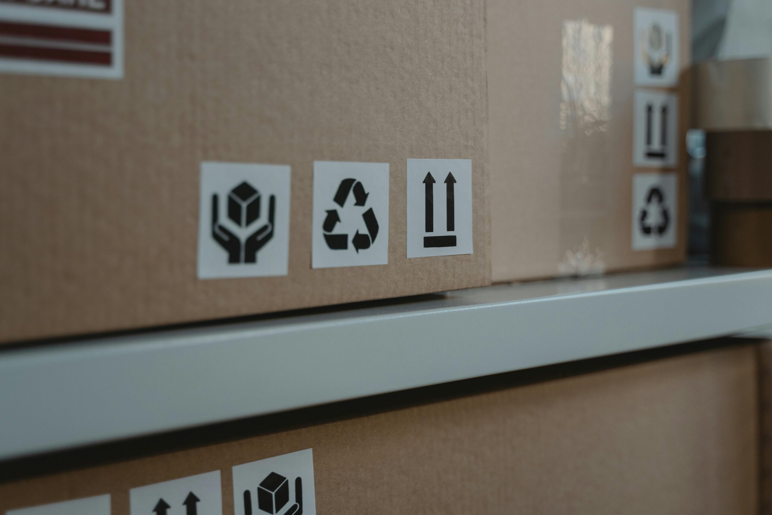 pexels-photo-6169028-6169028 Close-up of cardboard boxes displaying shipping and recycling symbols, ideal for logistic themes.