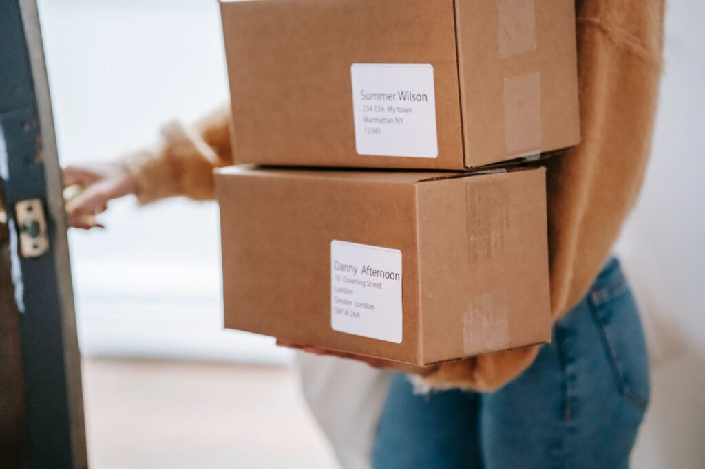 pexels-photo-6348105-6348105 Crop anonymous female wearing casual outfit carrying carton parcels with address labels opening door of post office