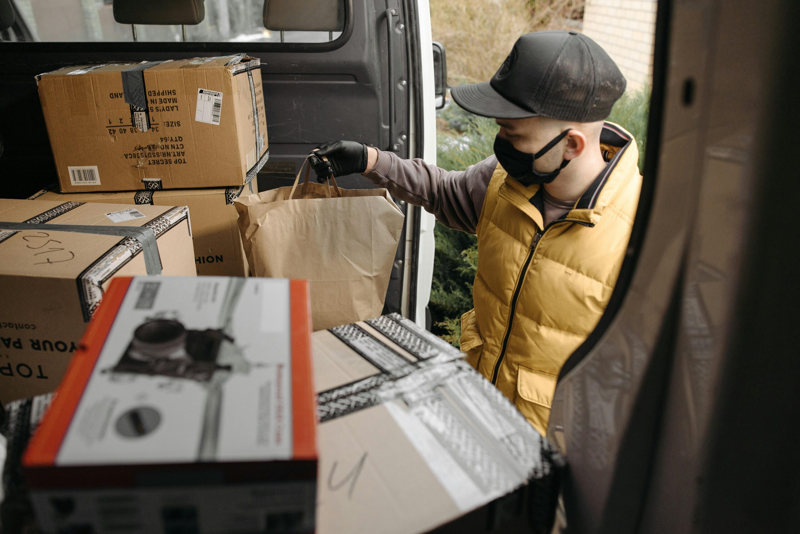 pexels-photo-6407556-6407556 A masked deliveryman loads packages into a van, illustrating modern logistics.