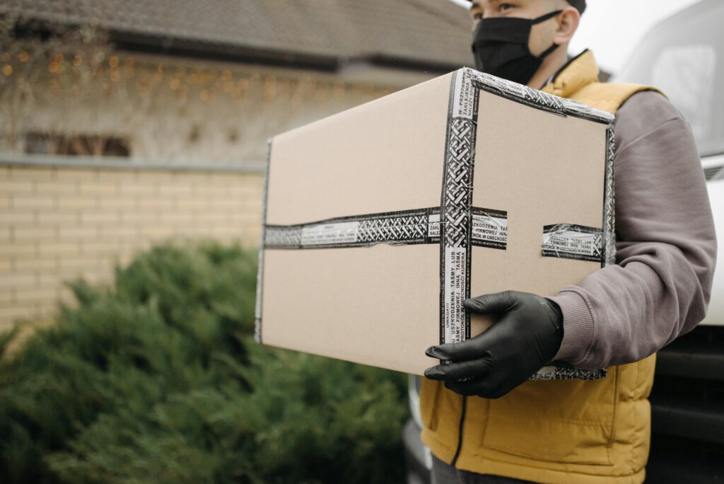 pexels-photo-6407568-6407568 Courier with mask and gloves delivering a package outdoors, embracing the new normal.