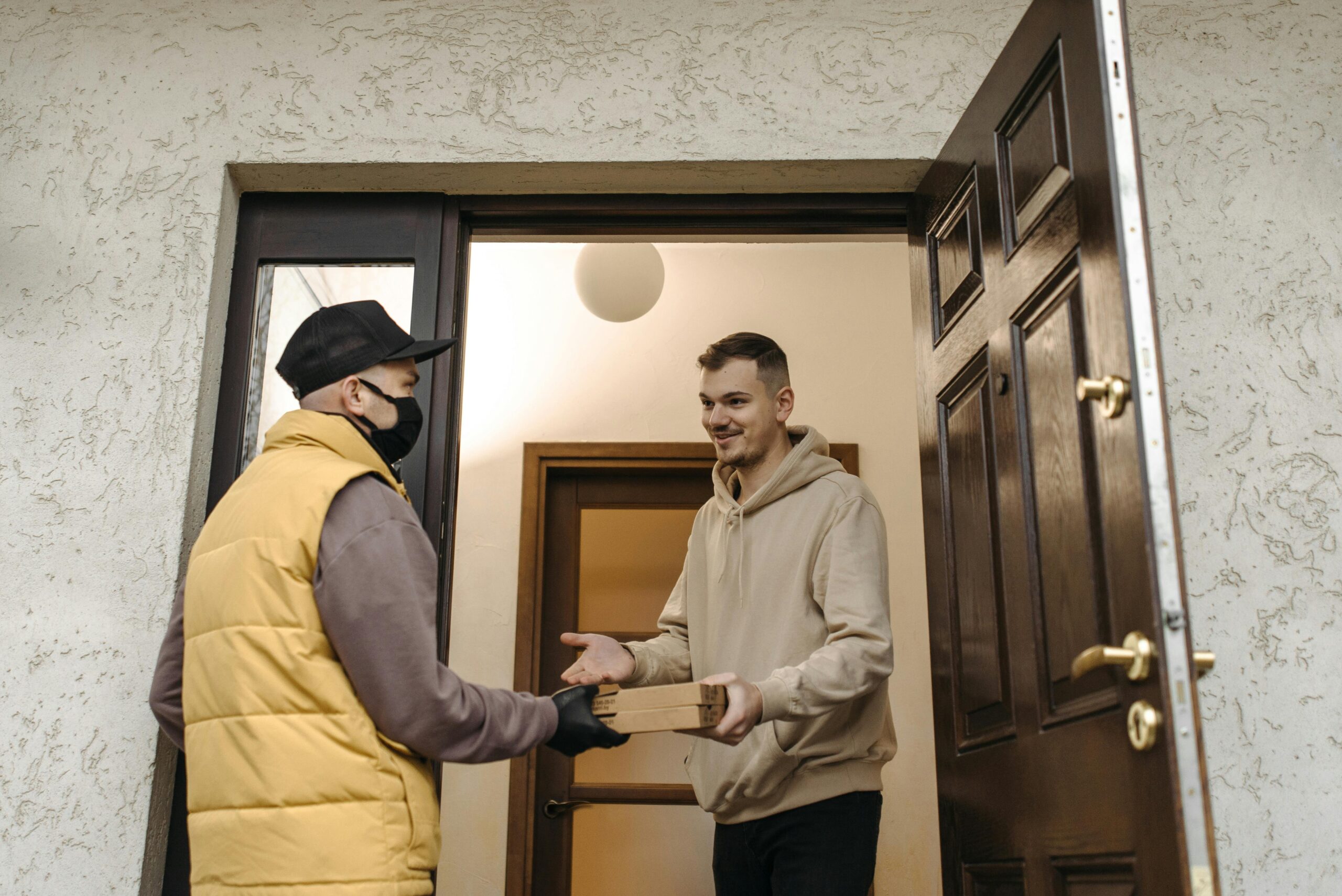 pexels-photo-6407620-6407620 A deliveryman with a facemask delivers a package to a man at the door.