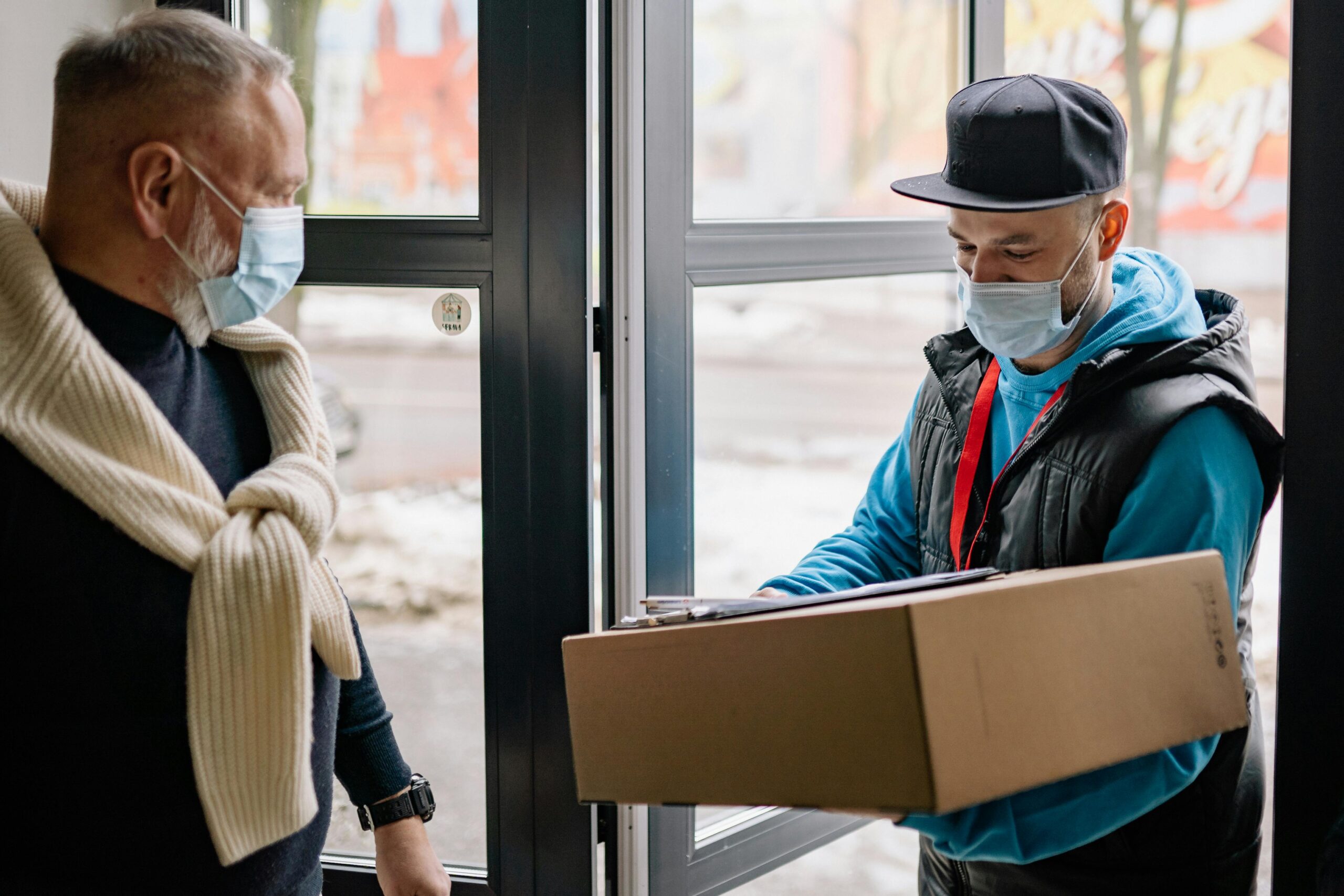 pexels-photo-6818157-6818157 Masked delivery service during pandemic, showcasing contact-free parcel handover.