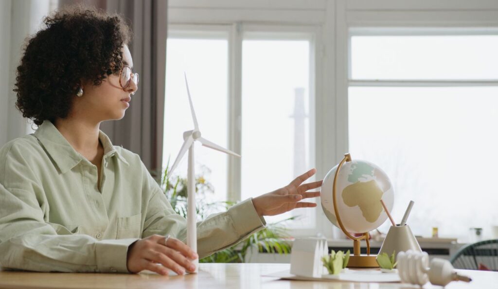 pexels-photo-6990475-6990475 A young woman explores renewable energy with a globe and wind turbine model indoors.