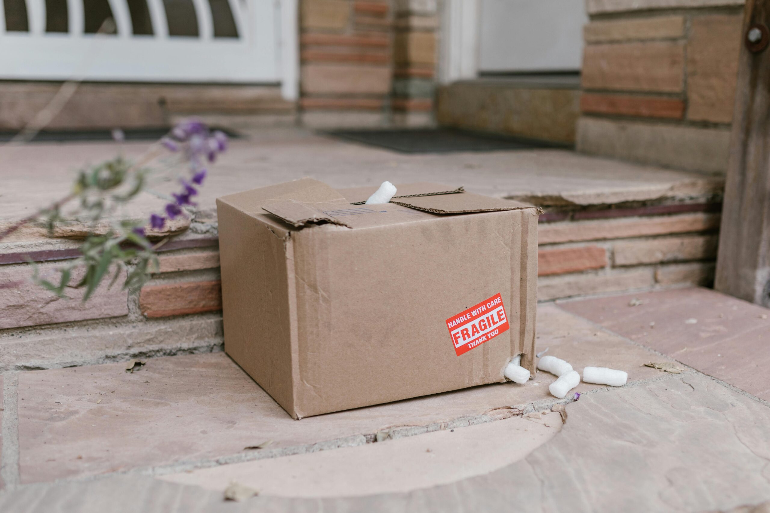 pexels-photo-7363092-7363092 Damaged cardboard package with fragile sticker on porch steps with foam peanuts.