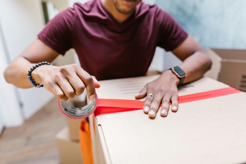 A man applying tape to a cardboard box for moving indoors.