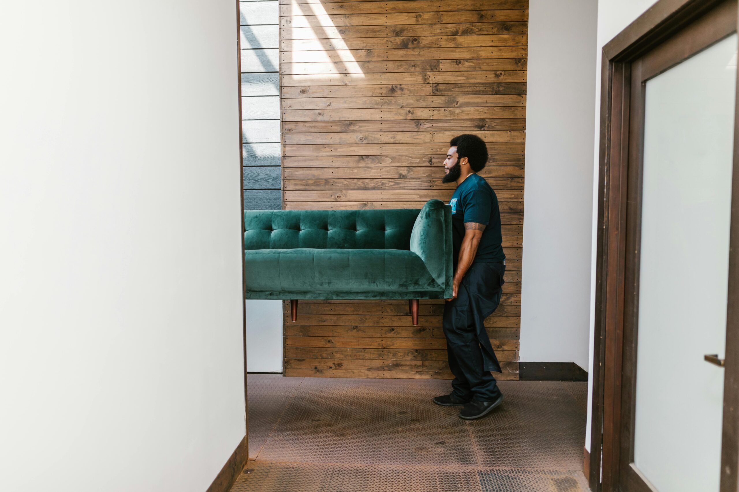 pexels-photo-7464722-7464722 A mover carries a green sofa indoors, showcasing modern interior design and relocation services.