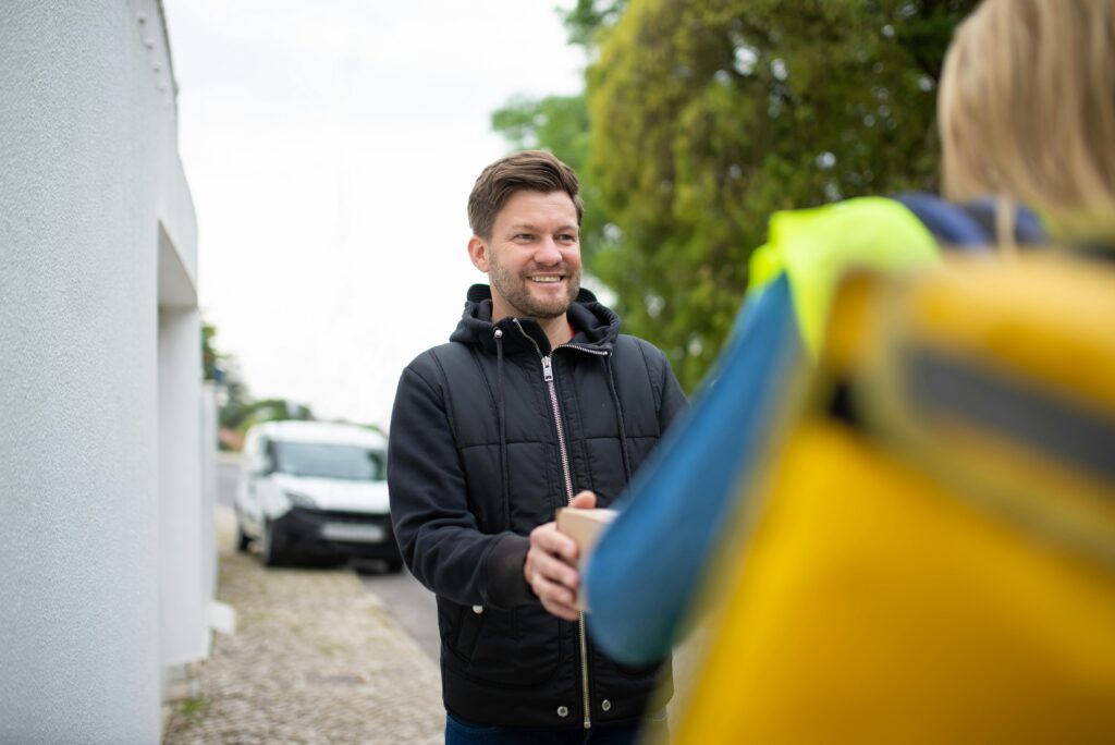 Smiling man receives a package from a delivery person outdoors in a friendly exchange.