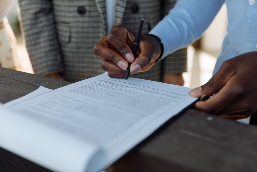 pexels-photo-8470831-8470831 Close-up of business professionals signing a document with a pen indoors.