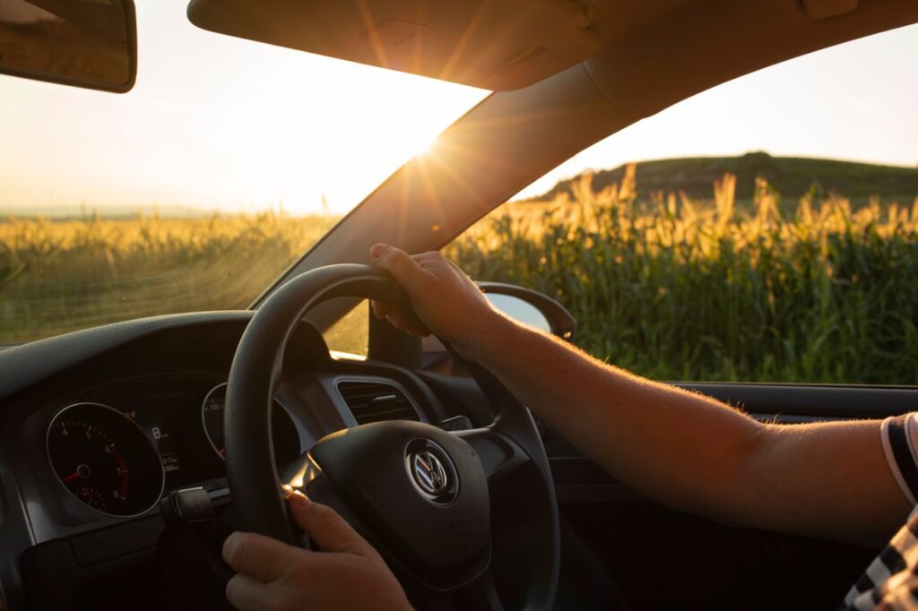 pexels-photo-9476491-9476491 A driver's view of a countryside road at sunset, focusing on the steering wheel.